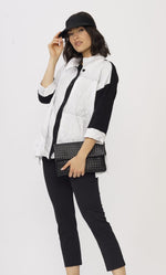 Load image into Gallery viewer, Front top half view of a model wearing the luukaa black and white crinkle shirt. This top has a striped wave print on it, black trim on the button down front, black sleeves with white cuffs, and a shirt collar. The model is touching her visor hat and holding a black purse
