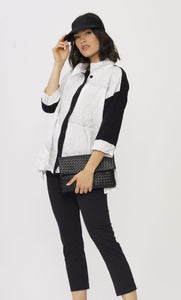 Front top half view of a model wearing the luukaa black and white crinkle shirt. This top has a striped wave print on it, black trim on the button down front, black sleeves with white cuffs, and a shirt collar. The model is touching her visor hat and holding a black purse