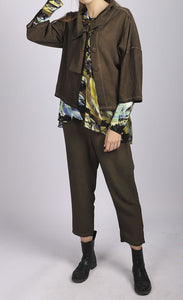 Front full body view of a woman wearing a brown jacket over a blue and green top. On the bottom she is wearing the luukka dyed tencel khaki pant. This pant is brown with a relaxed v-shape. It is also cropped.