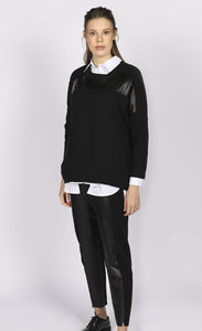 Front full body view of a woman wearing the luukaa faux leather top. This top is black with long sleeves and faux leather trim running horizontally across the top of the chest.
