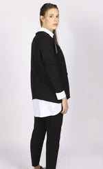 Load image into Gallery viewer, Back right side top half view of a woman wearing the luukaa faux leather top. This top is black with long sleeves and faux leather trim running horizontally across the top of the chest.
