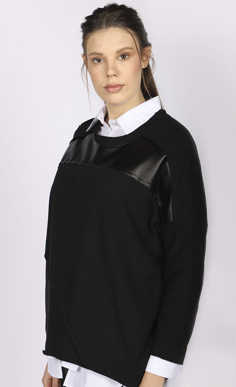 Front top half view of a woman wearing the luukaa faux leather top. This top is black with long sleeves and faux leather trim running horizontally across the top of the chest. 