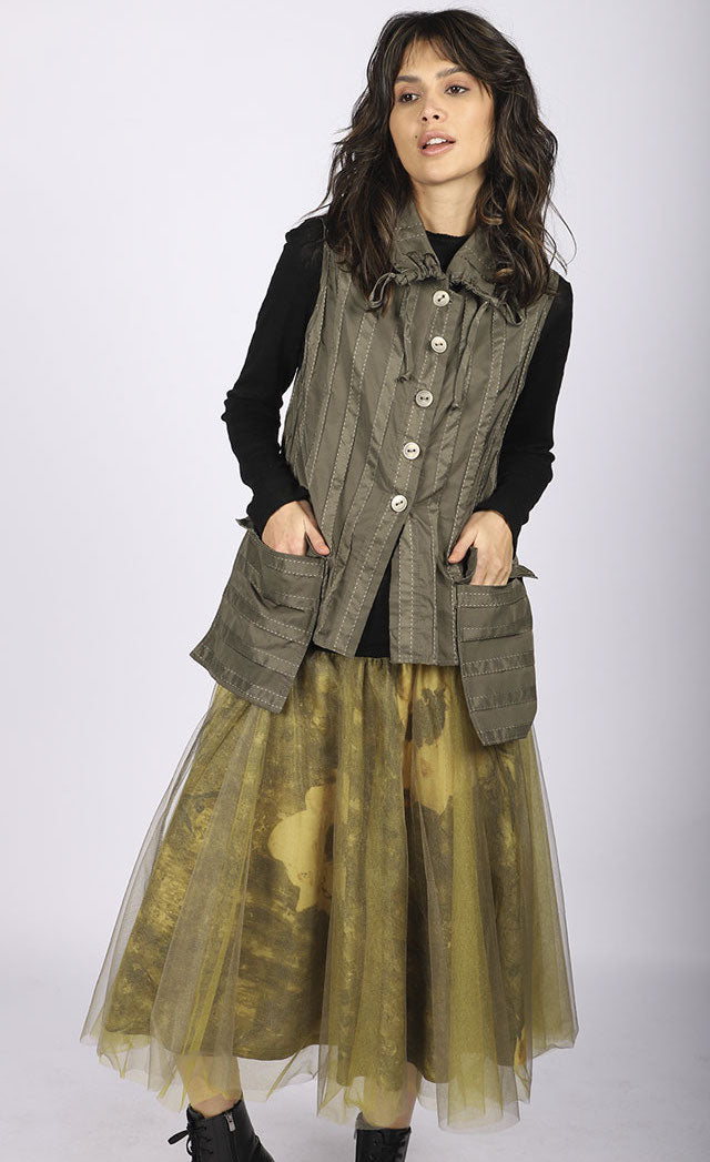 Front full body view of a woman wearing a brown vest over a black long sleeve top. On the bottom she is wearing the luukaa floral tulle skirt in khaki. This shirt has khaki tulle and a floral lining that shows through underneath. The skirt sits below the knees.