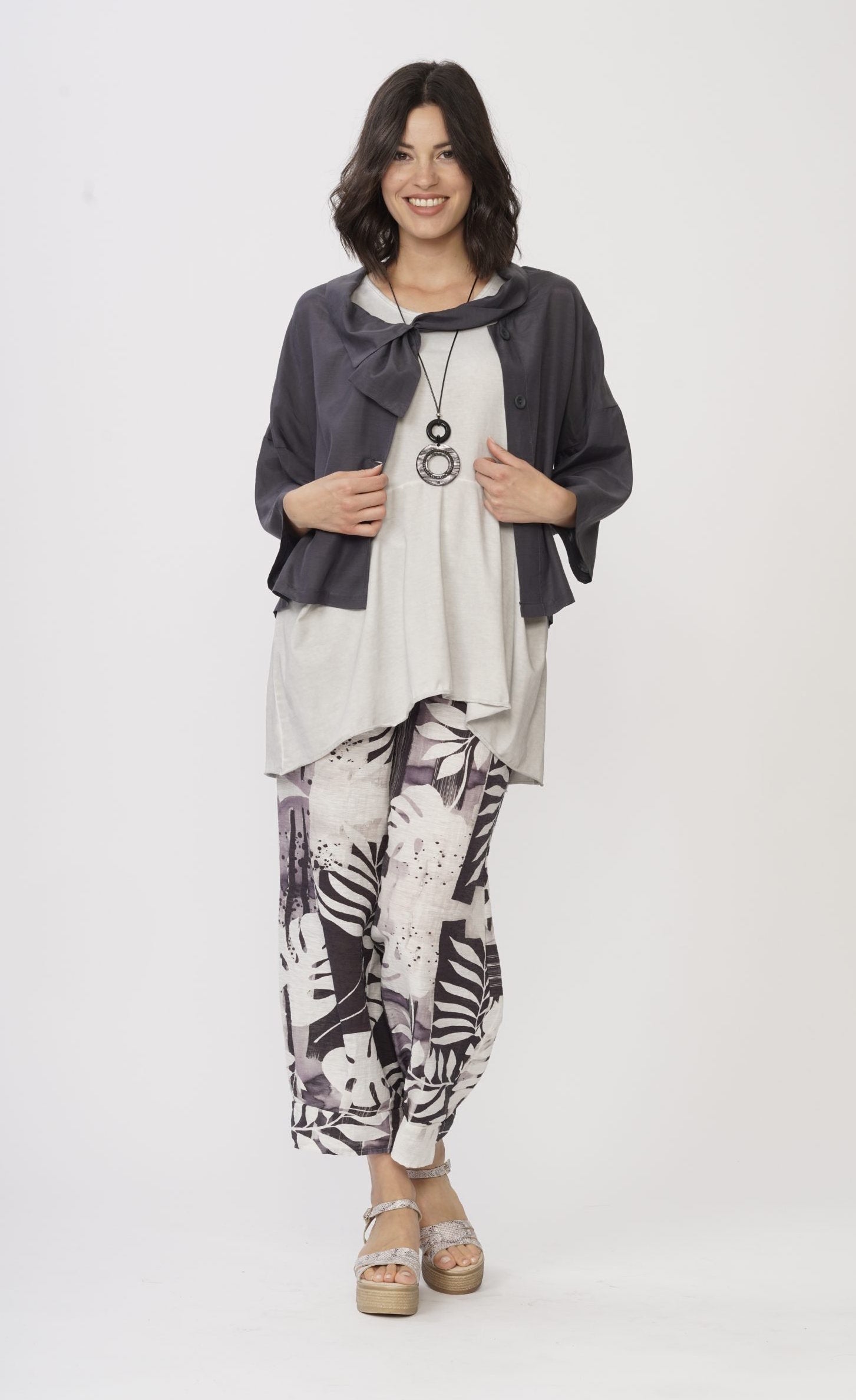 Front full body view of a woman wearing a white shirt with a grey jacket over it and the Luukaa Leaf Print Pant. The pant is wide leg with a white and lilac leaf print all over it.