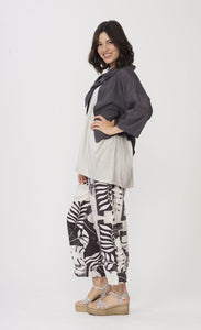 Left side full body view of a woman wearing a white shirt with a grey jacket over it and the Luukaa Leaf Print Pant. The pant is wide leg with a white and lilac leaf print all over it.