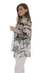 Load image into Gallery viewer, Left side top half view of a woman wearing white capris and the luukaa leaf print top. This top is sheer with white and grey leaf print. The sleeves are 3/4 length and the hem is short in the front and long on the sides and back.

