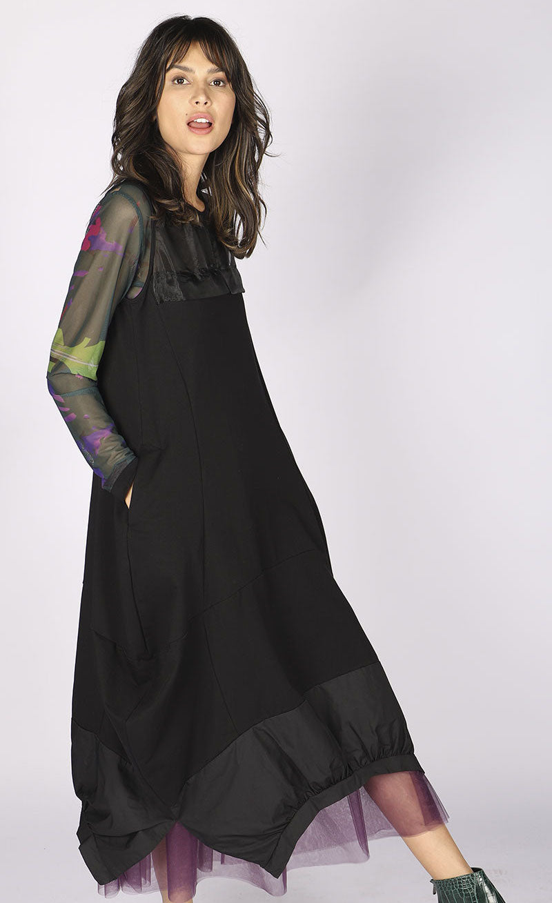 Right side full body of a woman wearing the luukaa long sleeveless dress. This dress is black with a tulle neckline and a structured fabric hem. The dress balloons out near the bottom.