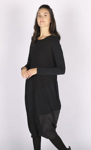 Front right side view of a woman wearing the black luukaa mixed media dress. This dress has long sleeves, a crew neck, and a mix of different black fabrics. The dress has extra space around the body with a tapered hem.