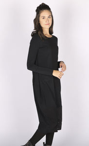 Left side view of a woman wearing the black luukaa mixed media dress. This dress has long sleeves, a crew neck, and a mix of different black fabrics. The dress has extra space around the body with a tapered hem.