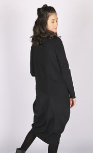 Back view of a woman wearing the black luukaa mixed media dress. This dress has long sleeves, a crew neck, and a mix of different black fabrics. The dress has extra space around the body with a tapered hem.