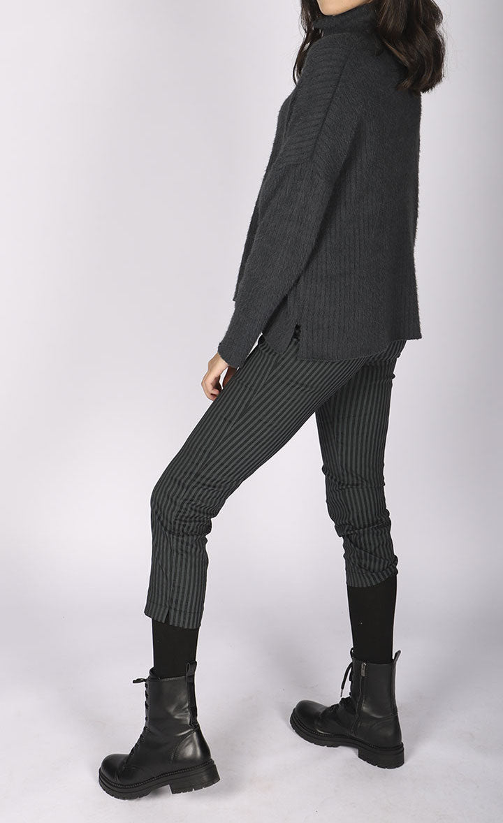 left side full body view of a woman wearing a grey sweater and the luukaa striped lycra pant. This slim pant has a cropped cut and grey and black vertical striping.