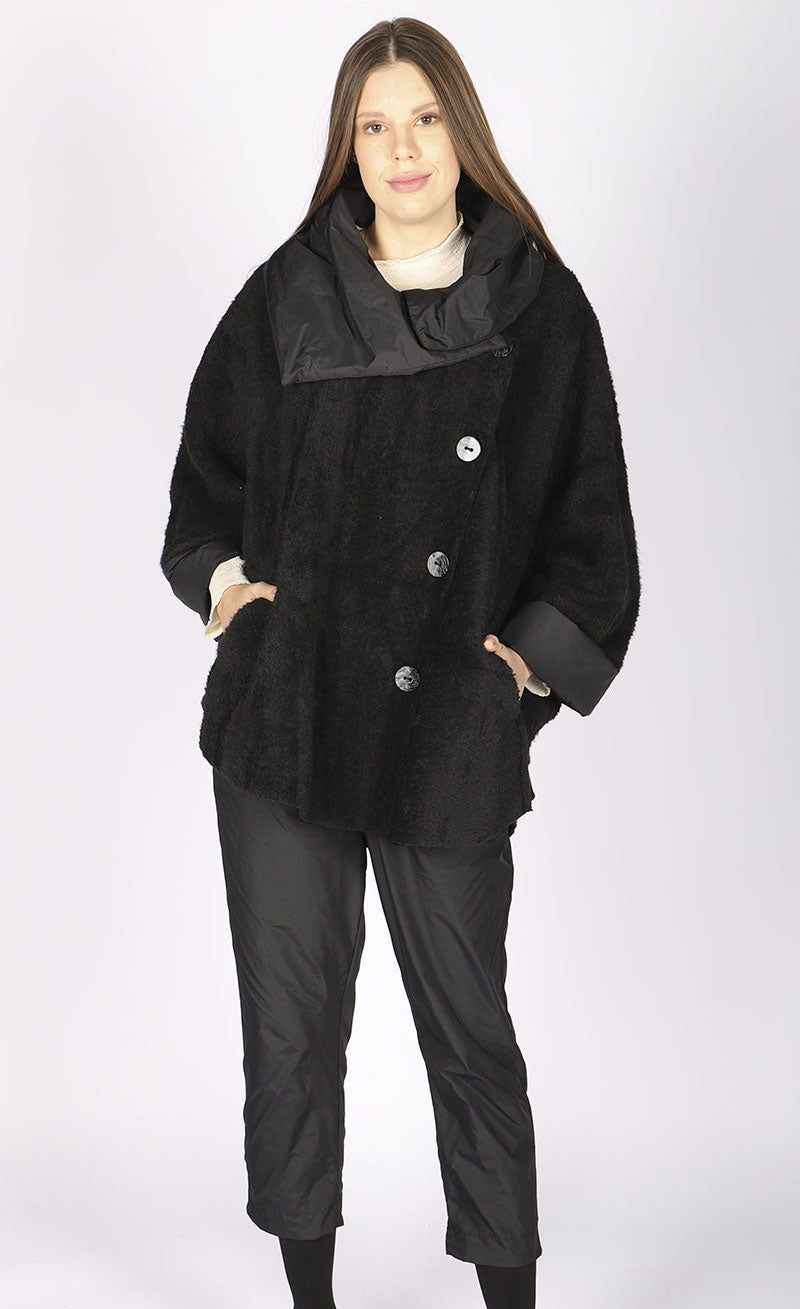 Front full body view of a woman wearing black pants and the luukaa black short coat. This coat is oversized with off center buttons running down the front, a wide collar, and fluffy looking black fabric.