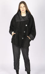 Load image into Gallery viewer, Front full body view of a woman wearing black pants and the luukaa black short coat. This coat is oversized with off center buttons running down the front, a wide collar, and fluffy looking black fabric.
