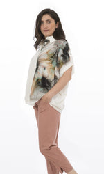 Load image into Gallery viewer, Left side, top half view of a woman wearing pink capris and the Luukaa Watercolor Shirt. This shortsleeve, white shirt has a button down front and shirt collar. The left side of the shirt has a watercolor print on it.
