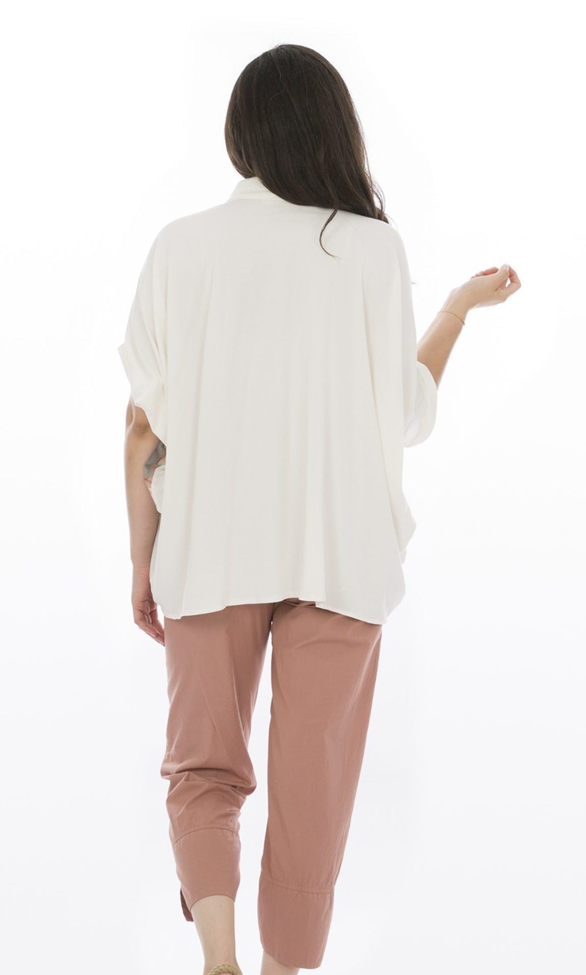 Back, top half view of a woman wearing pink capris and the Luukaa Watercolor Shirt. The back of this shirt is completely white and oversized. The sleeves are short and dolman-like.