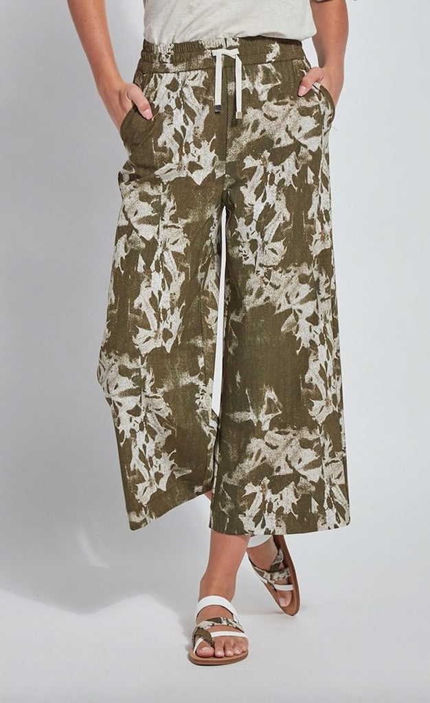 front Bottom half view of a woman wearing the lysse lila crop pant. This pant is green/khaki with a tie dye tropical floral white print. The waistband is elasticized with a drawstring front.