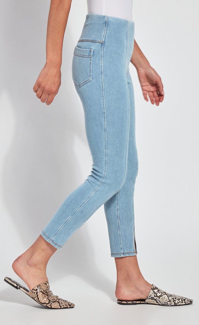 Right side, bottom half view of a woman wearing the Lysse Evelyn Split Denim Leggings. These leggings are a light wash with seams running down the center, back pockets, and a small front slit at the bottom.