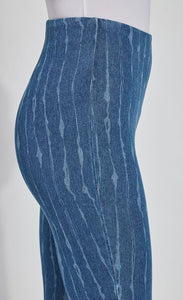 Side close up view of a woman wearing the lysse lynette scallop edge denim pattern legging. The leggings are a mid-wash denim color with white streaks running vertically down the leg. The pants are high-waisted.
