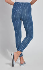 Load image into Gallery viewer, Back bottom half view of a woman wearing the lysse lynette scallop edge denim pattern legging. The leggings are a mid-wash denim color with white streaks running vertically down the leg. The pants are high-waisted.
