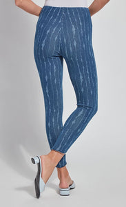 Back bottom half view of a woman wearing the lysse lynette scallop edge denim pattern legging. The leggings are a mid-wash denim color with white streaks running vertically down the leg. The pants are high-waisted.