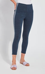 Load image into Gallery viewer, Front view of the bottom half of a woman with her hands in the back pocket of her Lysse Nomad Crop Leggings. These leggings are dark denim with a side blue and white houndstooth printed stripe going down the entire leg. The leggings cut off above the ankles and the woman is wearing flat beige sandals.
