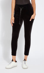 Load image into Gallery viewer, Front bottom half view of a woman wearing the lysse nook velvet jogger. This black jogger is body hugging like a legging with side pockets and a high-waisted tie waistband.
