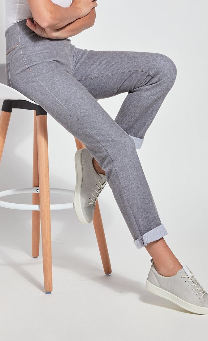 Side bottom half view of a woman sitting on a stool with one leg stretched out and wearing the Lysse Boyfriend Denim pants. These pants are grey, cuffed, and have a straight leg.