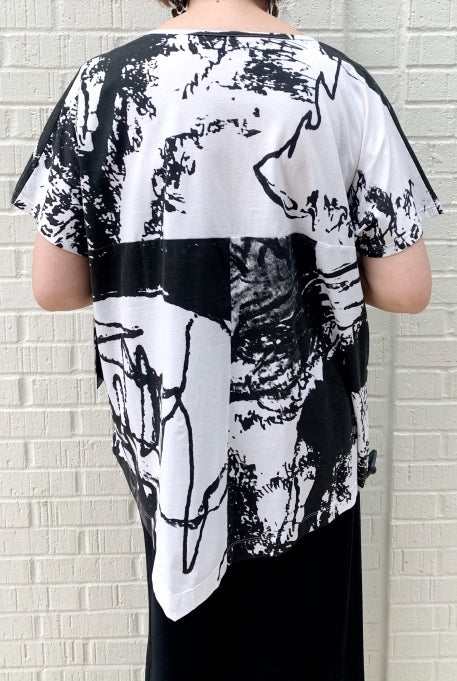 Back top half view of a woman wearing the moyuru short sleeve printed top. This top is white with black abstract print and an asymmetrical hem.
