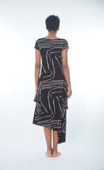 Load image into Gallery viewer, Back full body view of a woman wearing the matthidul safari muse dress. This dress is black with an abstract taupe print on it. The dress has cap sleeves and an asymmetrical hem.
