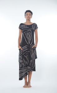 Front full body view of a woman wearing the matthidul safari muse dress. This dress is black with an abstract taupe print on it. The dress has cap sleeves, front pockets, and an asymmetrical hem.