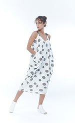 Load image into Gallery viewer, Front full body view of a woman wearing the m x matthildur trapeze dress. This dress is sleeveless with black elastic straps. This dress is white/ivory with black dots all over it. The front has two front pockets and a v-neck.
