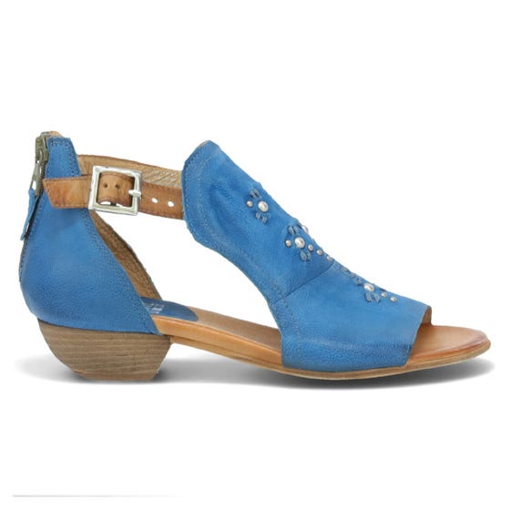 Outer side view of the miz mooz canary sandal in the color denim. This sandal has an open toe, a mid-heel, a buckle strap around the ankle, and exposed sides.