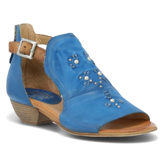 Front outer side view of the miz mooz canary sandal in the color denim. This sandal has an open toe, a mid-heel, a buckle strap around the ankle, and exposed sides.