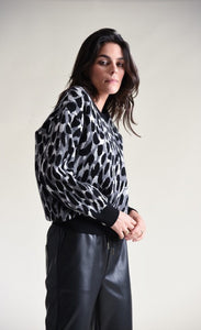 Front top half view of a woman wearing black pants and the molly bracken animal print sweater. This sweater has grey, black, and with animal print with black trim on the cuffs, hem, and round neckline.