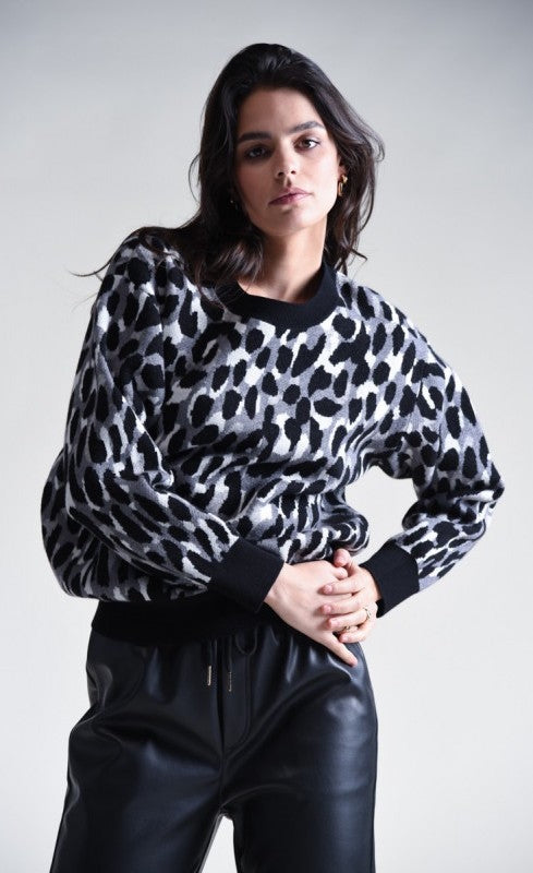 Front top half view of a woman wearing black pants and the molly bracken animal print sweater. This sweater has grey, black, and with animal print with black trim on the cuffs, hem, and round neckline.