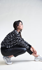 Load image into Gallery viewer, Right side full body view of a woman crouching down and wearing black pants and the molly bracken animal print sweater. This sweater has grey, black, and with animal print with black trim on the cuffs, hem, and round neckline.
