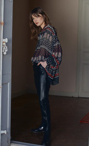 Front full body view of a woman wearing black leather pants and the molly bracken tzigane print shirt. This shirt has a mix of black, white, and red prints, a button down front, an oversized fit, and balloon sleeves.