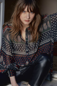 Front top half view of a woman wearing the molly bracken tzigane print shirt. This shirt has a mix of black, white, and red prints, a button down front, an oversized fit, and balloon sleeves.