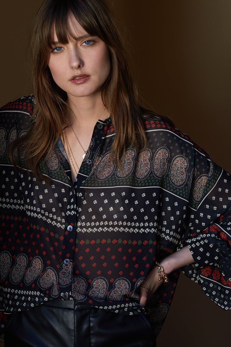 Front top half view of a woman wearing the molly bracken tzigane print shirt. This shirt has a mix of black, white, and red prints, a button down front, an oversized fit, and balloon sleeves.
