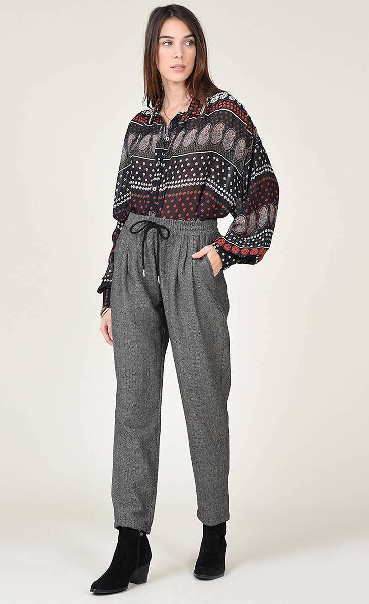 Front full body view of a woman wearing the molly bracken tzigane print shirt and the molly bracken grey herringbone pant. This pant has an elastic waistband with a black tie and a wider fit with legs that taper in at the bottom.