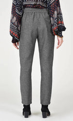 Load image into Gallery viewer, Back bottom half view of a woman wearing the molly bracken tzigane print shirt and the molly bracken grey herringbone pant. This pant has an elastic waistband with a black tie and a wider fit with legs that taper in at the bottom.
