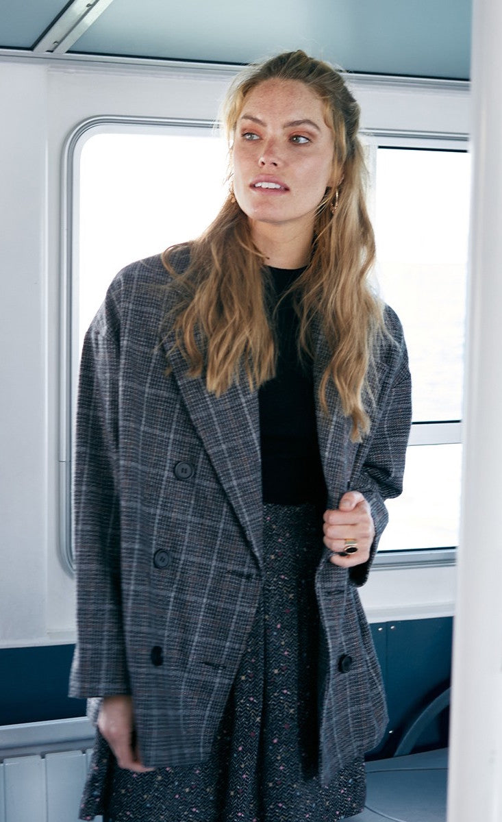 Front top half view of a woman wearing the molly bracken plaid caban coat. This oversized coat is grey with double breasted buttons and a large collar.
