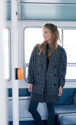 Load image into Gallery viewer, Front full body view of a woman wearing the molly bracken plaid caban coat and a skirt with tights. This oversized coat is grey with double breasted buttons and a large collar.
