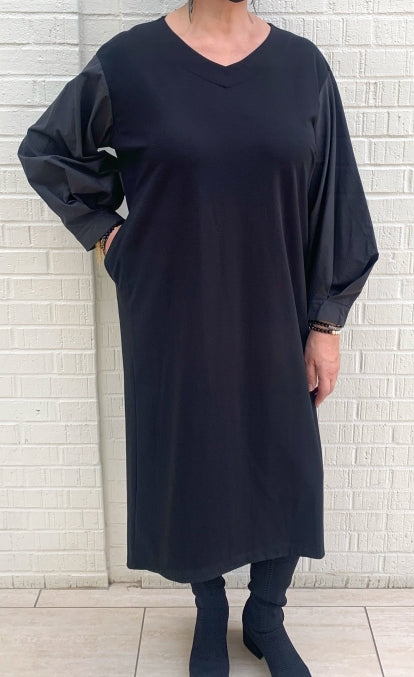 Front full body view of a woman wearing the moyuru black dress. This dress hits below the knees and has a straight silhouette, oversized long sleeves made of a structured fabric, and a v-neck.