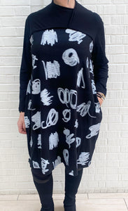 front full body view of a woman wearing the moyuru black and white scribble dress. This dress is solid black on the sleeves and black with white scribble print on the body. This dress also has long sleeves and an asymmetrical neck.