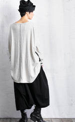 Load image into Gallery viewer, Back full body view of a woman wearing black pants and the moyuru light grey scribble top. This top is solid light grey/white with a contrasting black stitching running vertically down the middle. The top has long sleeves and a round neck.
