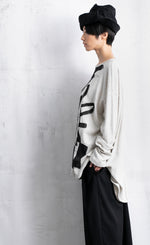 Load image into Gallery viewer, Left side top half view of a woman wearing black pants and the moyuru light grey scribble top. This top is light grey/white colored with an abstract black print all over the front. The top has long sleeves and a round neck.
