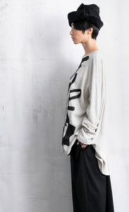 Left side top half view of a woman wearing black pants and the moyuru light grey scribble top. This top is light grey/white colored with an abstract black print all over the front. The top has long sleeves and a round neck.