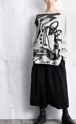 Load image into Gallery viewer, Front full body view of a woman wearing black pants and the moyuru light grey scribble top. This top is light grey/white colored with an abstract black print all over the front. The top has long sleeves and a round neck.
