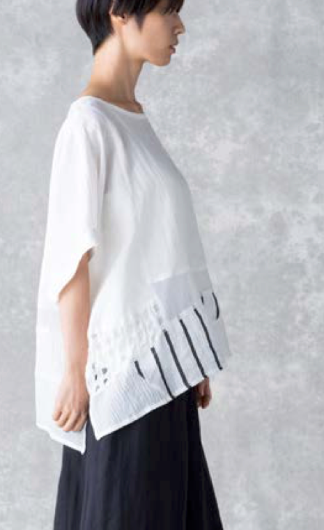 Right sided top half view of a woman wearing the moyuru white short sleeve top. This top features a round neck and an asymmetrical hem with layered striped, solid, and dotted fabric.